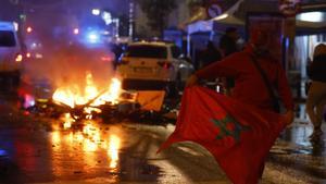 Un aficionado con la bandera de Marruecos en una calle de Bruselas con un foco de incendio al fondo.