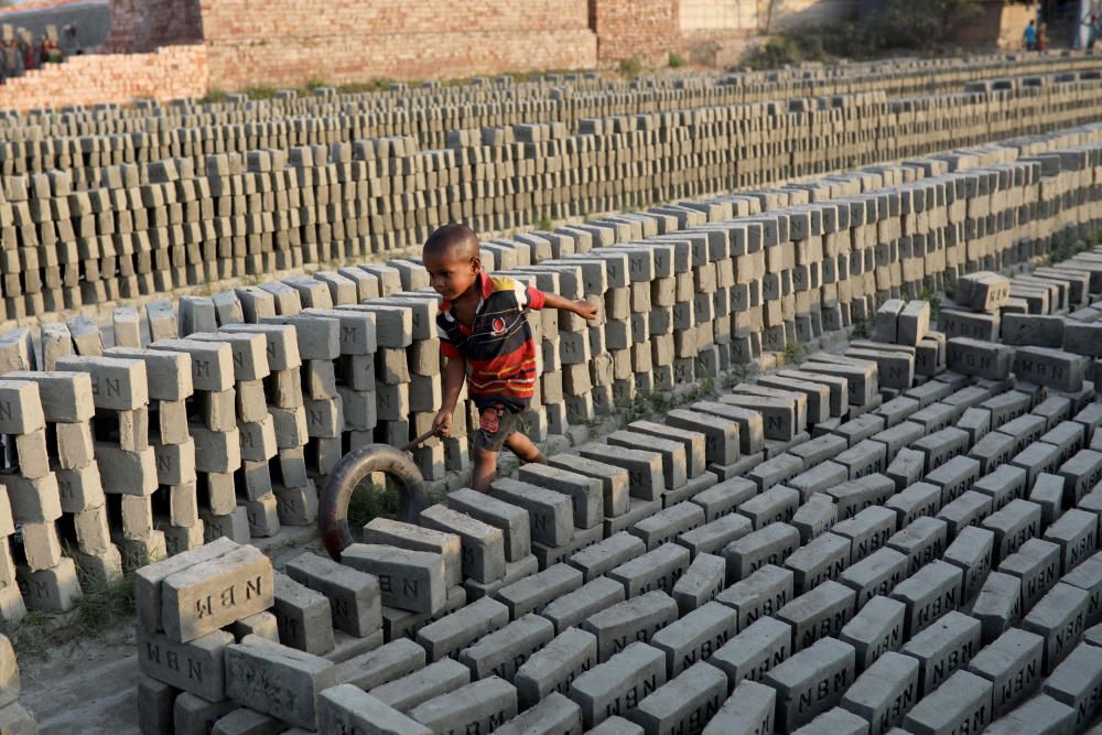A child plays with a tire in a brick factory in ...