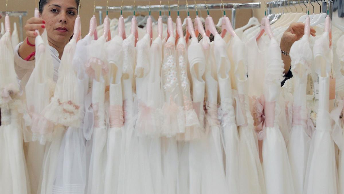 GRAFCVA4628. VALENCIA, 10/05/2019.- Una mujer revisa vestidos de comunión en el Día Mágico by FIMI, única feria internacional y profesional especializada en moda de comunión y ceremonia, que abre este viernes sus puertas en Feria Valencia, con 140 marcas y propuestas de diferentes estilos, desde el clásico al moderno, pasando por el romántico, boho-chic, bohemio, vintage e incluso unisex. EFE/ Kai Försterling
