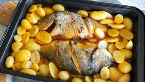 Un plato de besugo al horno sobre lecho de patatas.