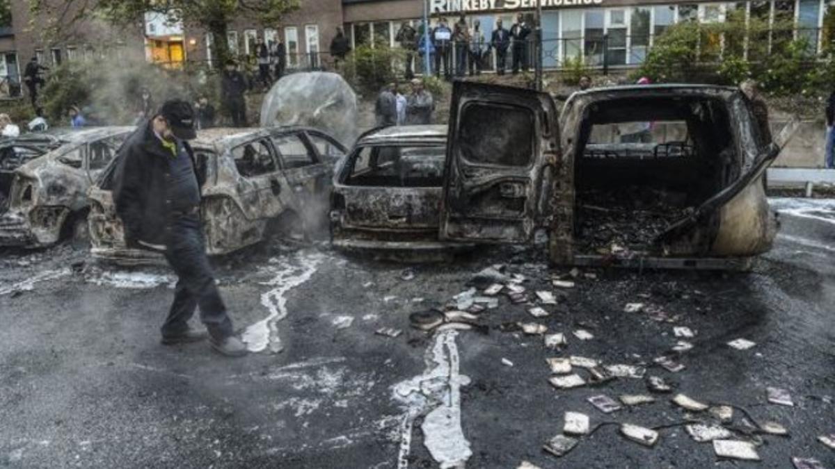 Un hombre camina junto a una hilera de coches carbonizados tras unos disturbios en mayo del 2013, en un suburbio de Estocolmo.