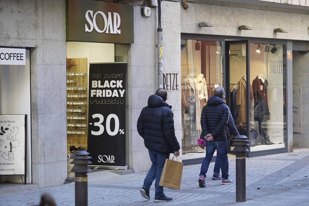Diverses persones passen per davant d’un aparador amb ofertes pel Black Friday al centre de Girona.