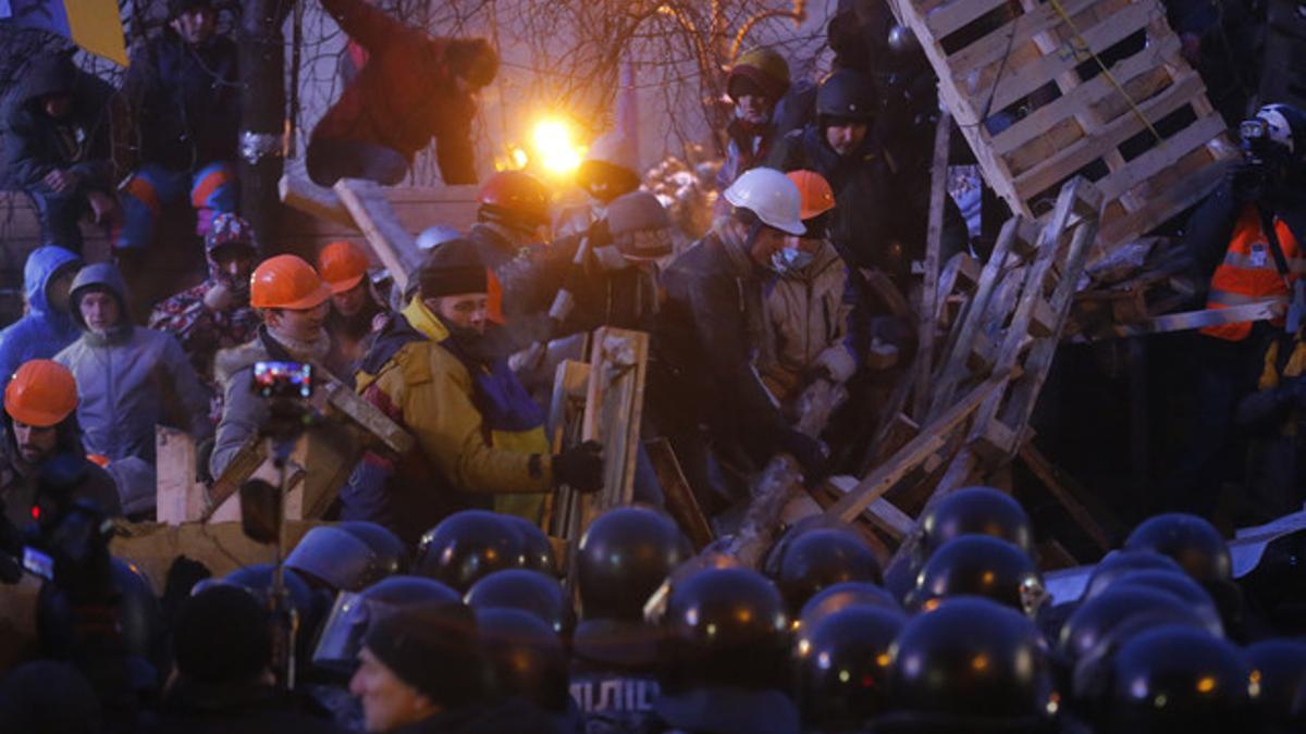 Un grupo de manifestantes refuerzan una barricada frente a los antidisturbios, en la plaza de la Independencia de Kiev.