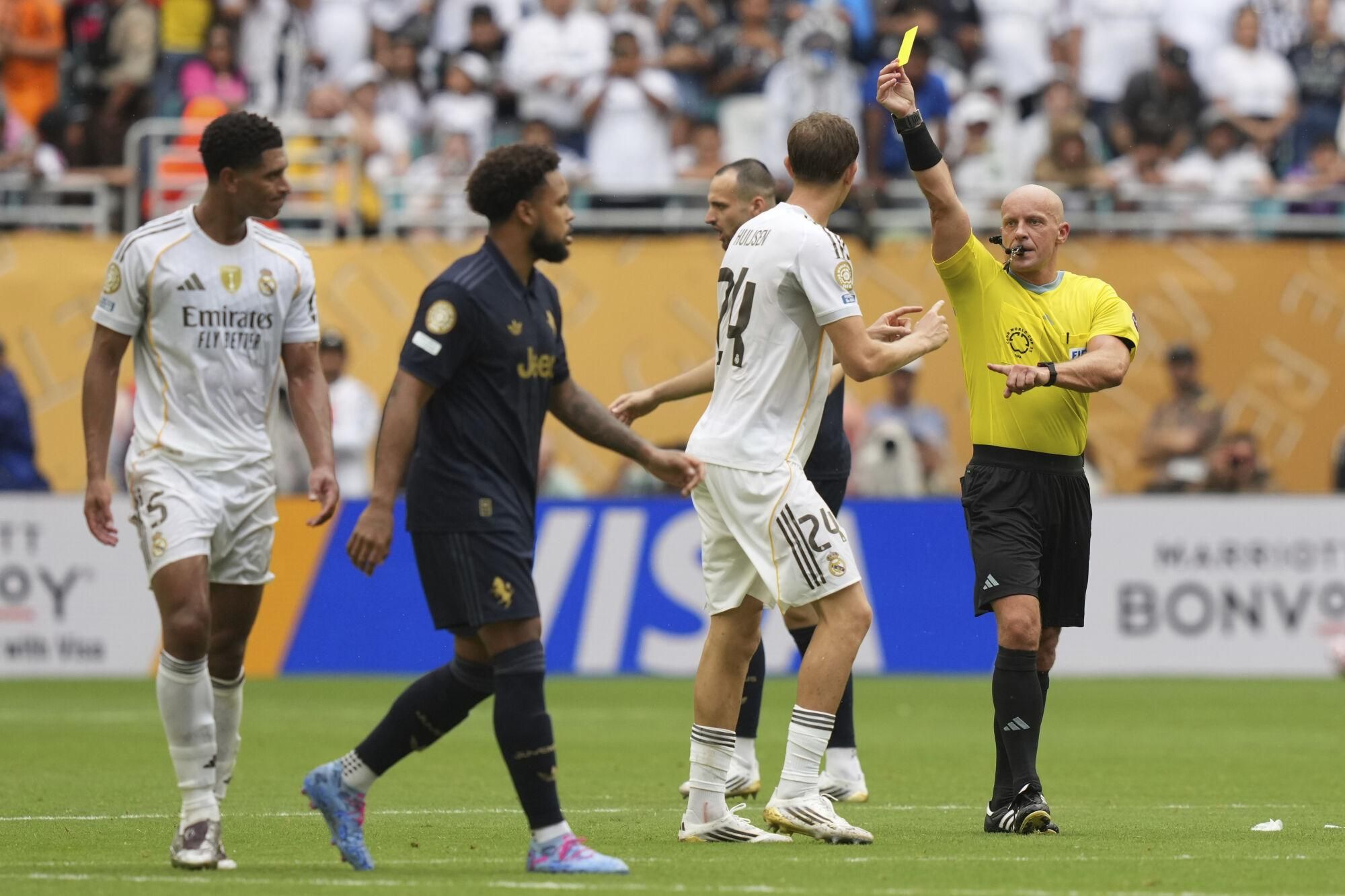 Referee Szymon Marciniak shows the yellow card to Real Madrid's Jude Bellingham, left, during the Club World Cup round of 16 soccer match between Real Madrid and Juventus in Miami Gardens, Fla., Tuesday, July 1, 2025. (AP Photo/Lynne Sladky). EDITORIAL USE ONLY/ONLY ITALY AND SPAIN