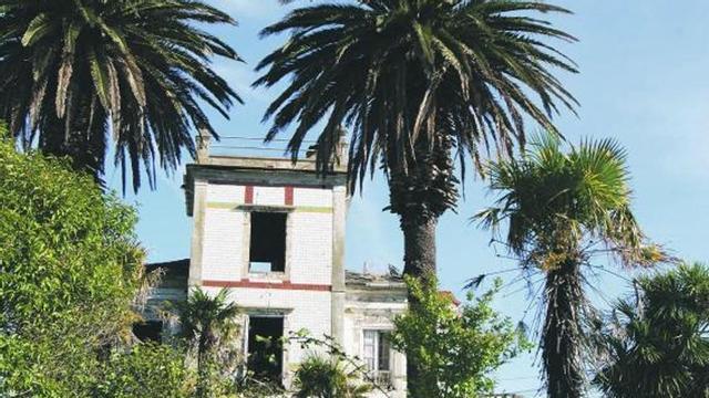 Paredes con más de un siglo. En la imagen superior, la fachada principal flanqueada por dos palmeras, fieles acompañantes de los edificios de la arquitectura indiana. Sobre estas líneas, detalle de la fachada, donde se aprecia la belleza del inmueble y también su grave deterioro.