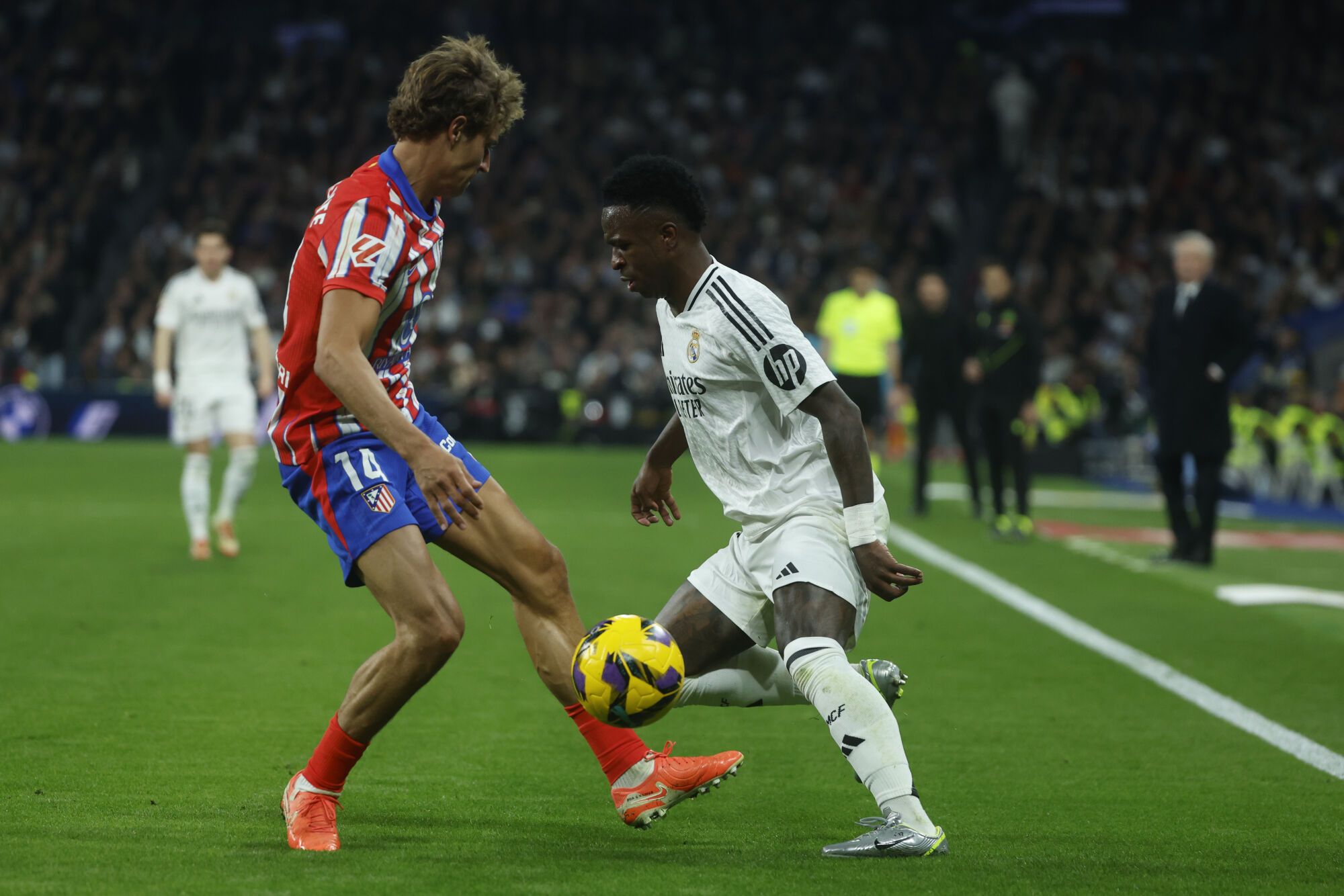 MADRID, 08/02/2025.- El delantero del Real Madrid Vinicius Jr. (d) intenta escaparse de Marcos Llorente, del Atlético de Madrid, durante el partido de la jornada 23 de LaLiga de fútbol que Real Madrid y Atlético de Madrid disputan este sábado en el estadio Santiago Bernabéu. EFE/Juanjo Martín
