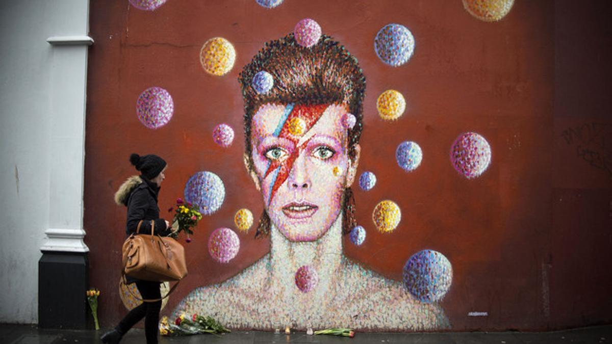 Una chica deposita flores frente a un mural de David Bowie en Brixton, Londres