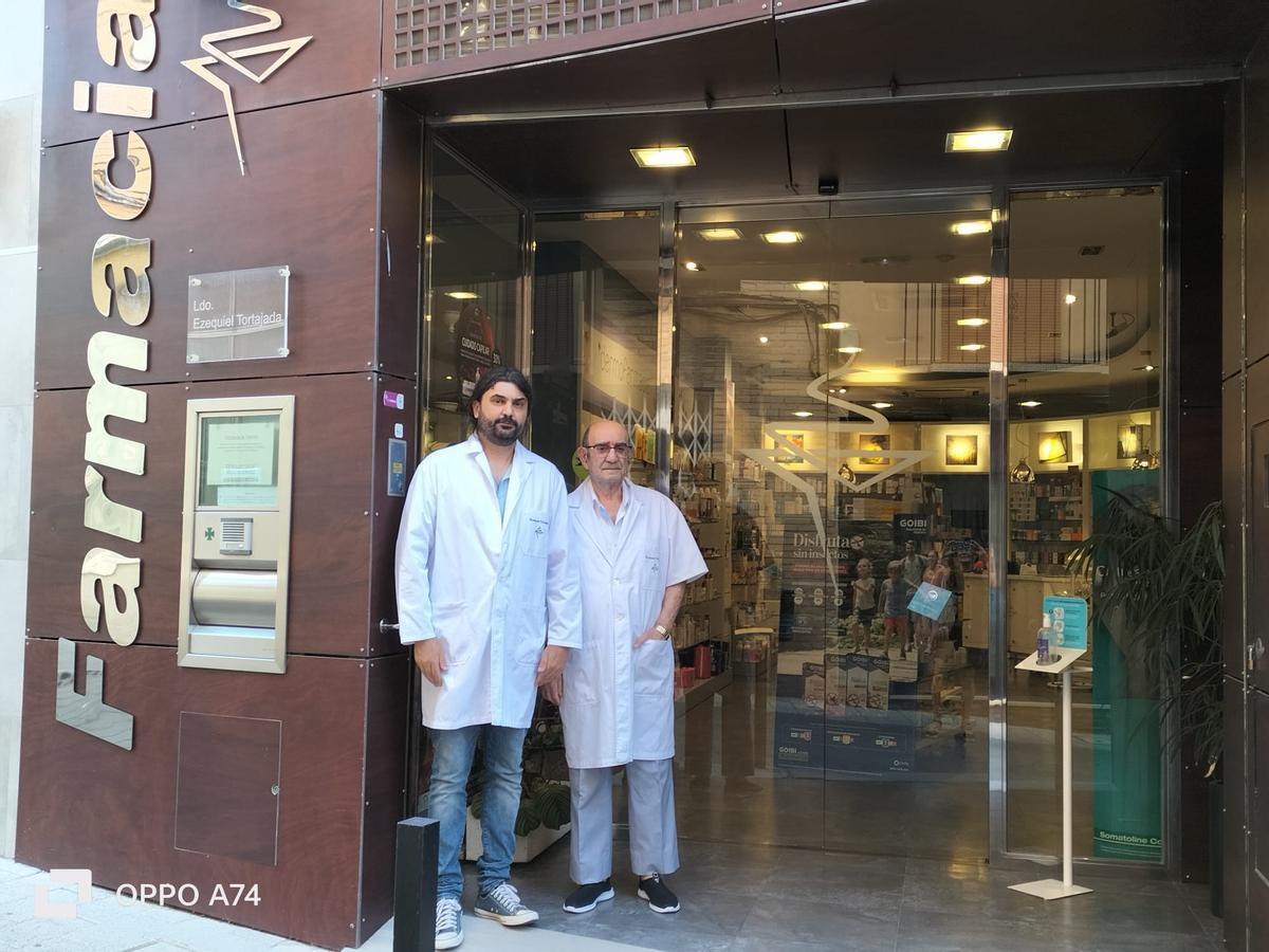 Ezequiel Tortajada padre e hijo en la fachada de la farmacia que ha pasado por tres generaciones.