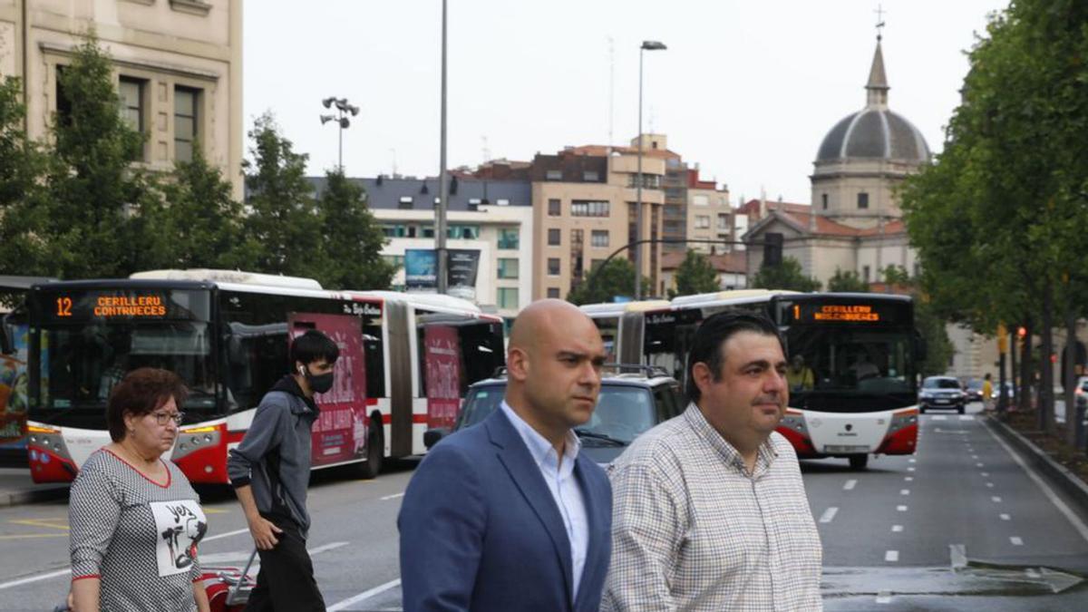 Los concejales foristas Jesús Martínez Salvador y Pelayo Barcia cruzan un paso de peatones en la plaza del Humedal, con autobuses de Emtusa detrás de ellos. | Marcos León