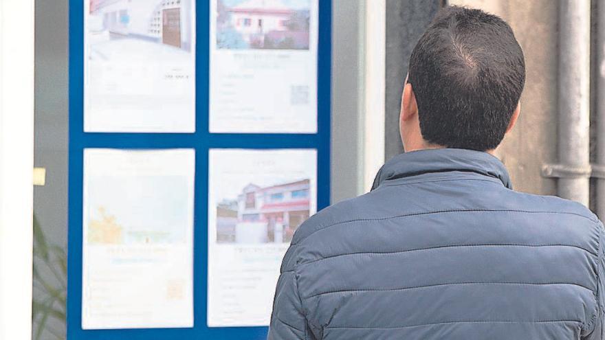 Un hombre consulta anuncios de casas en el escaparate de una inmobiliaria.