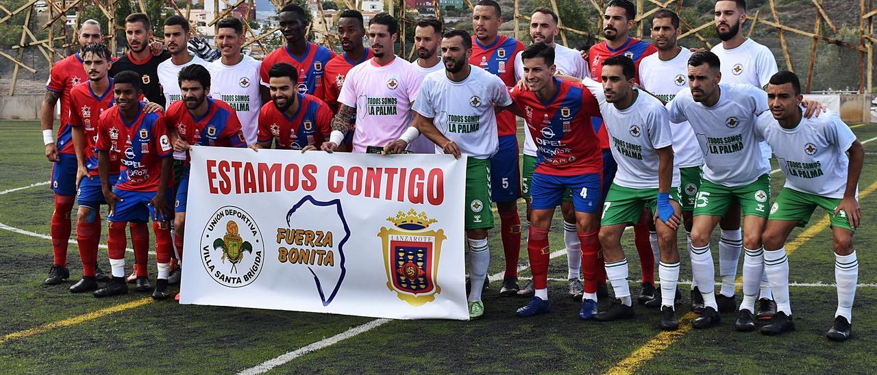 Los jugadores del Villa Santa Brígida y de la UD Lanzarote posan con una pancarta de ánimo a La Palma por la crisis vulcanológica que vive la isla. | | RAMÓN REGUERO