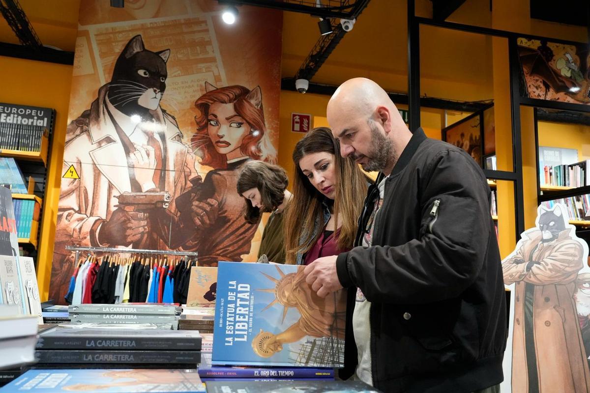Dos clientes hojean un ejemplar ante la atenta mirada de dos personajes de cómic.