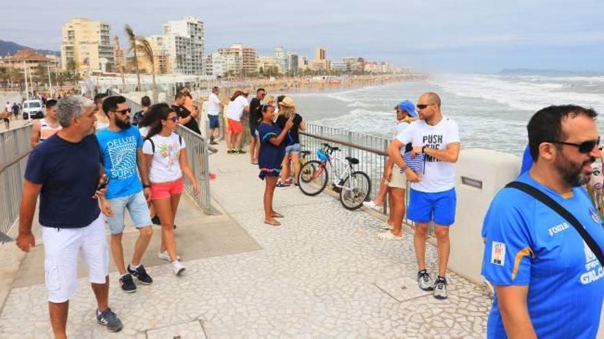 Varios turistas hacen fotos con su teléfono móvil en el paseo de la escollera de Gandia.