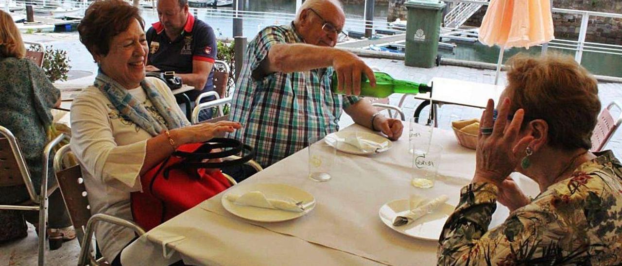 Manuel Torre echa culinos de sidra a Ángeles Vázquez y María Luisa Baragaño en el muelle candasín.