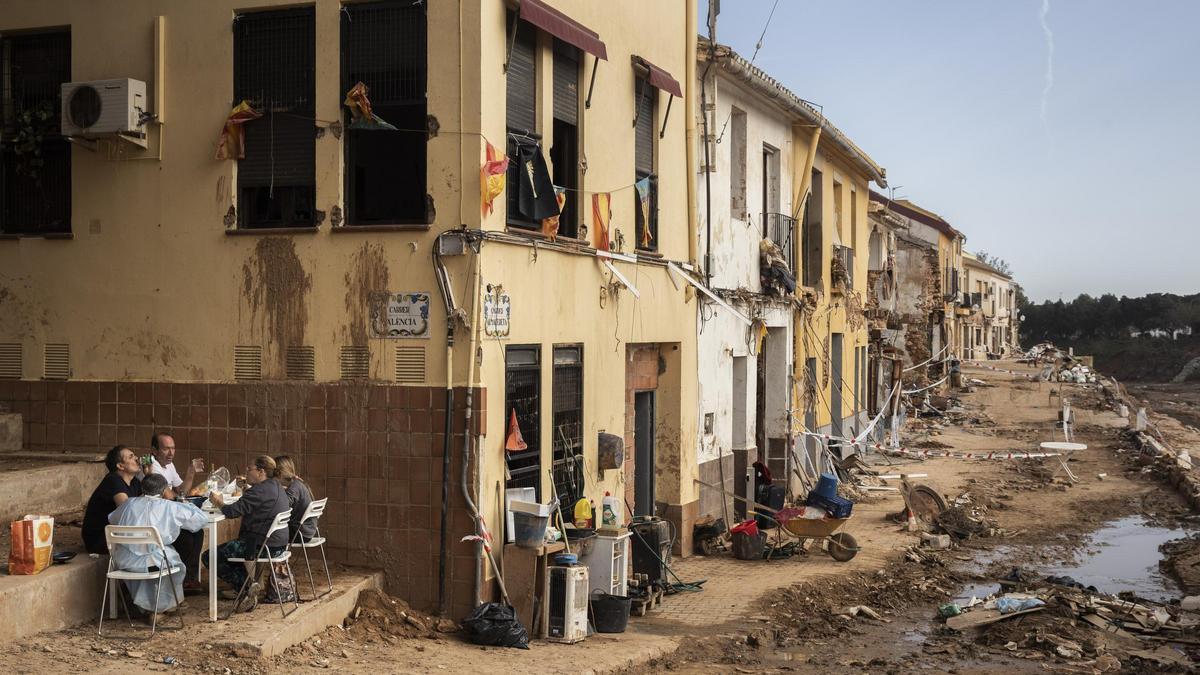Una familia come a los pies de su casa destrozada tras la dana, en un descanso de las largas jornadas de limpieza.