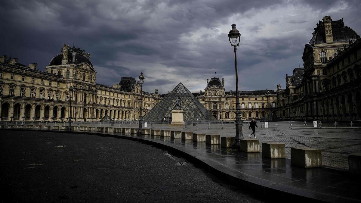 Una mujer pasa junto a la pirámide de cristal frente al Louvre en medio del cierre nacional debido al coronavirus.
