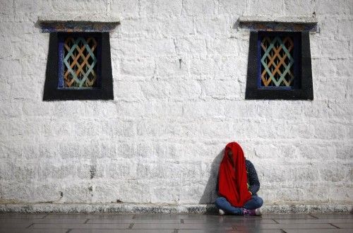 A woman in a red scarf rests in the sun outside Jokhang Monastery in Lhasa