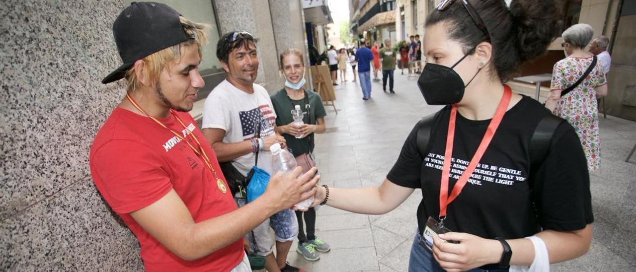 Ariadna Fernández da botellas de agua a varias personas por la calle Trapería de Murcia, ayer.