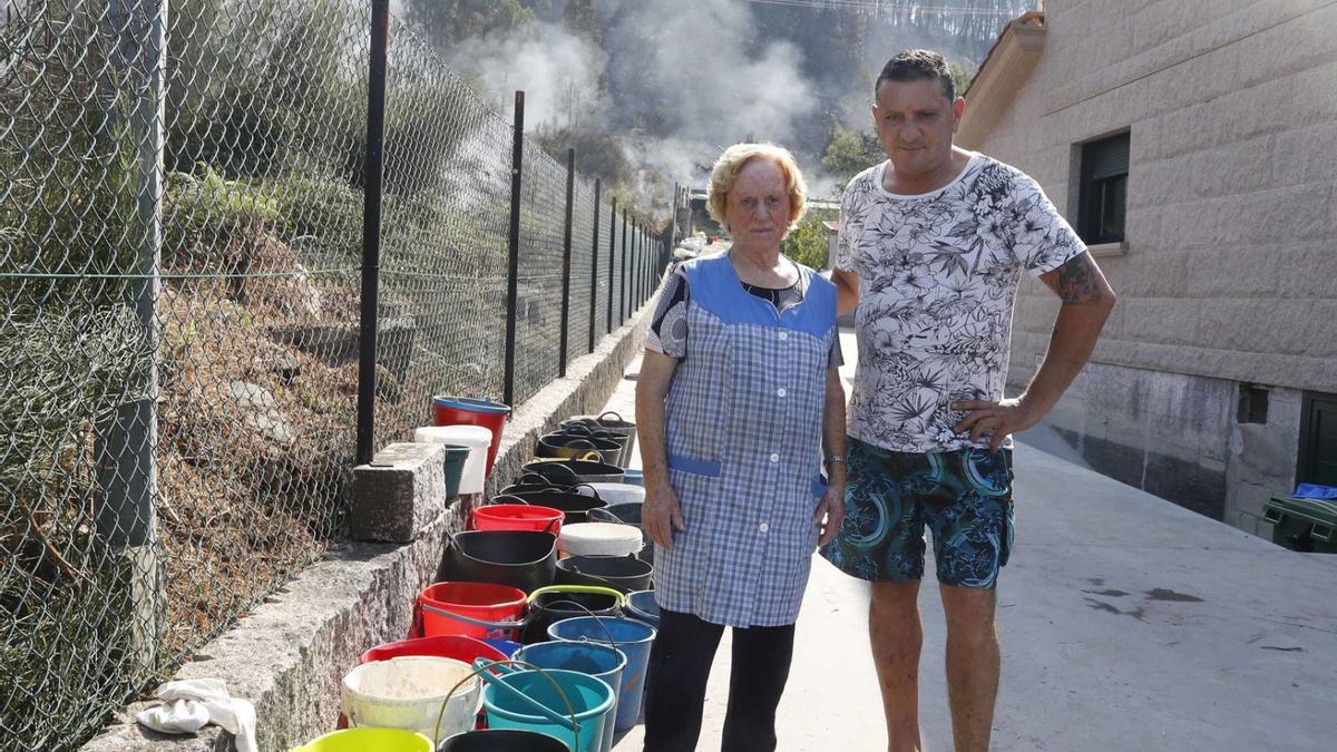 Orlando Rúa, con su madre y los cubos utilizados por los vecinos para apagar el         fuego.   | // PABLO HERNÁNDEZ 