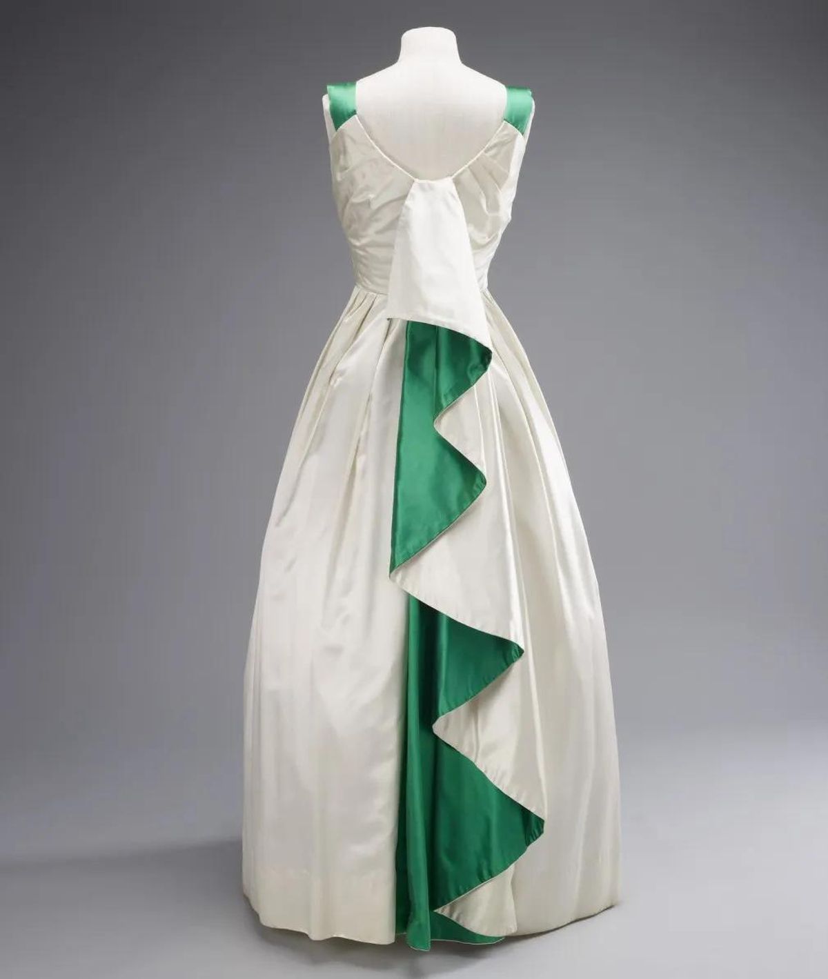 Ingenioso vestido blanco diseñado por Norman Hartnell para un banquete de Estado en Karachi en 1961, que incorpora los colores nacionales de Pakistán a través de un dramático pliegue verde esmeralda que cae en cascada por la espalda.