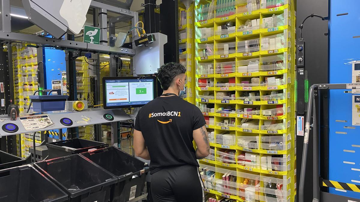 Un empleado de Amazon incorpora productos al almacén de Amazon en El Prat, frente a una estantería que protagoniza el 'caos ordenado' de las plantas logísticas automatizadas del gigante del comercio electrónico.
