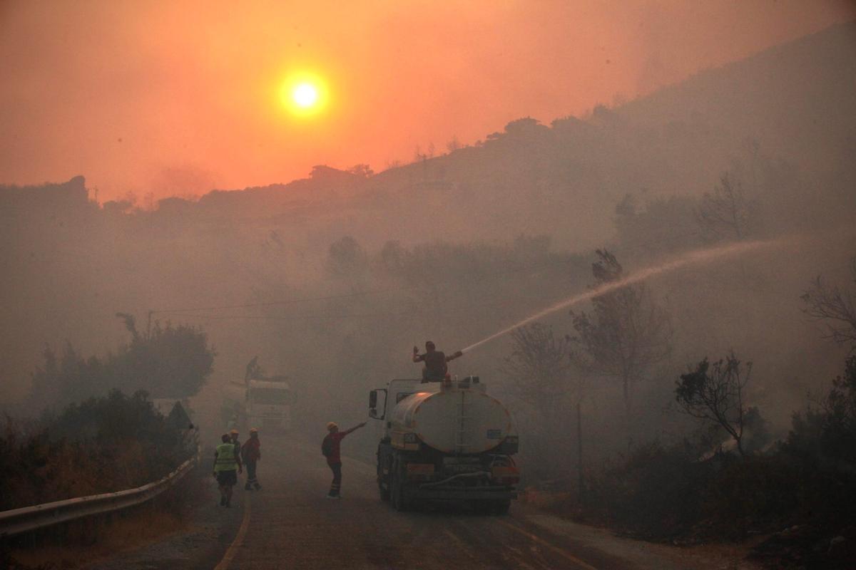 Bomberos, ayudados por ciudadanos voluntarios, trabajan para extinguir el fuego que se extiende por los alrededores de la ciudad de Oren, en la costa del Egeo, en Turquía.