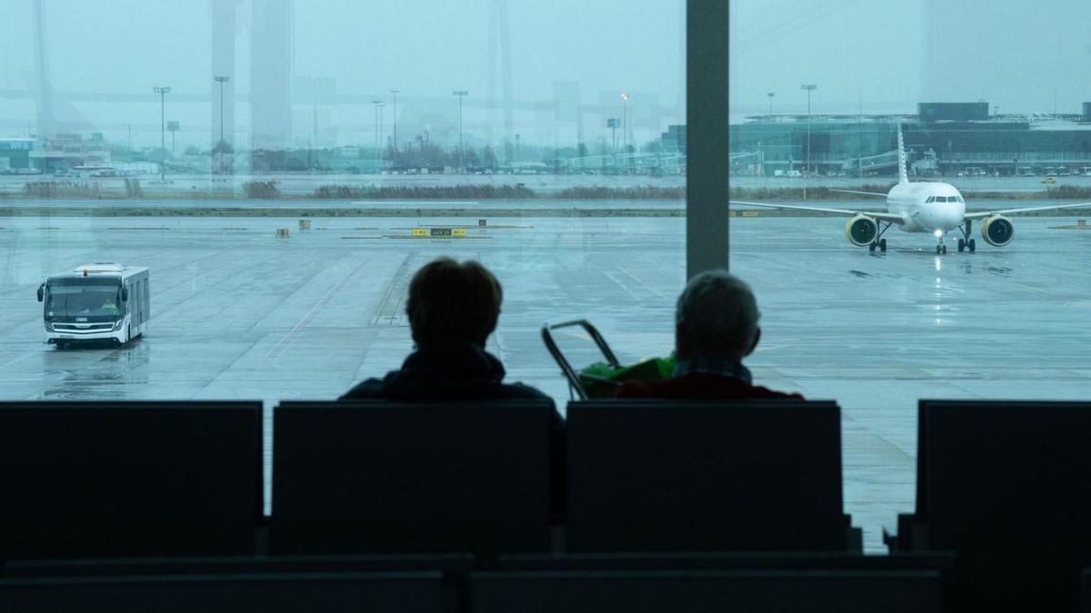 Dues persones esperen assegudes davant d’un avió a l’aeroport del Prat. | DAVID ZORRAKINO / EUROPA PRESS