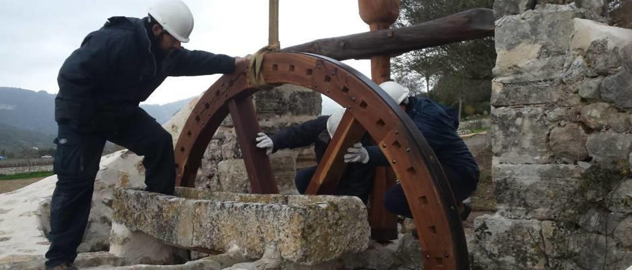 Operarios del taller de patrimonio instalan el mecanismo de madera a una antigua noria.