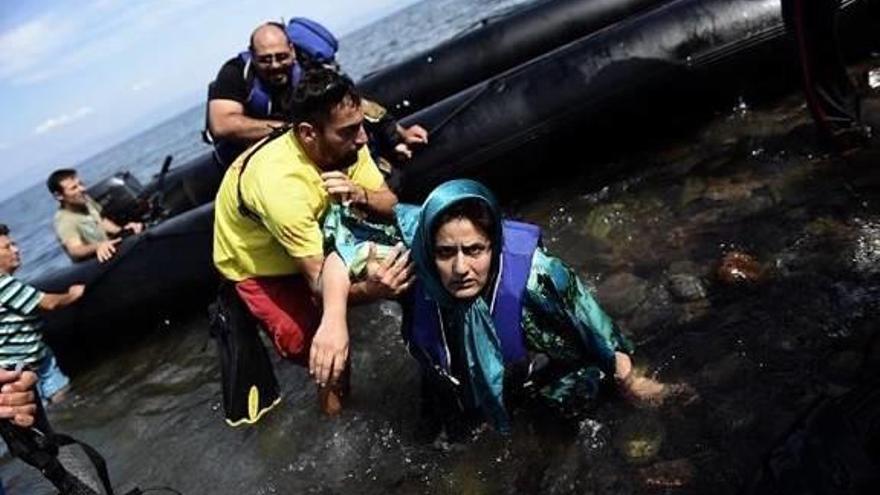 Una mujer cae al agua mientras es ayudada por un socorrista. A la derecha, una compañera suya tapa a una niña siria.