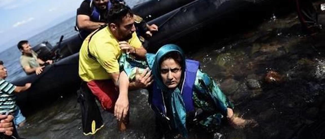 Una mujer cae al agua mientras es ayudada por un socorrista. A la derecha, una compañera suya tapa a una niña siria.