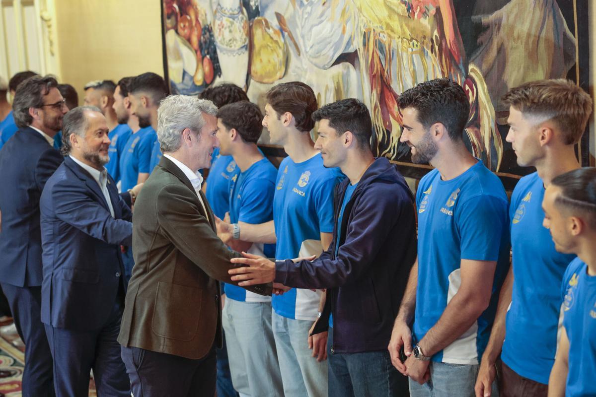 SANTIAGO DE COMPOSTELA, 26/05/2026.- El presidente de la Xunta, Alfonso Rueda (c), acompañado por el presidente del club, Juan Carlos Escotet, saluda a los miembros de la plantilla del Deportivo durante la recepción ofrecida tras su ascenso a Primera División, este martes en Santiago de Compostela. EFE/Lavandeira jr.