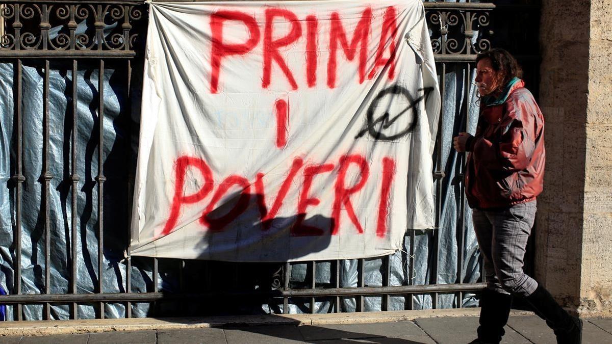 Angela Grossi, desalojada de una vivienda abandonada, pasa junto a una pintada en una sábana que reza 'Primero los pobres', colgada en el pórtico de la basílica de los Santos Apóstoles, en Roma, el 29 de enero.