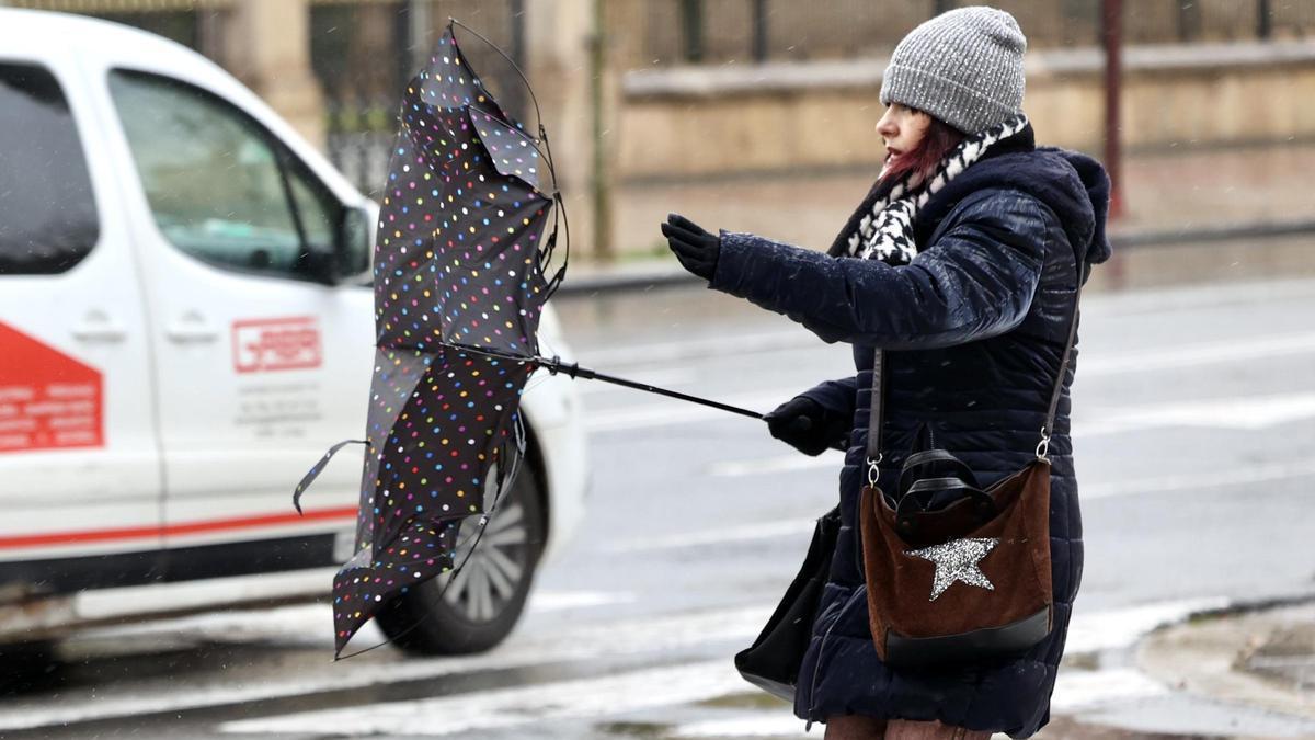 Una joven intenta evitar que el viento destroce su paraguas.