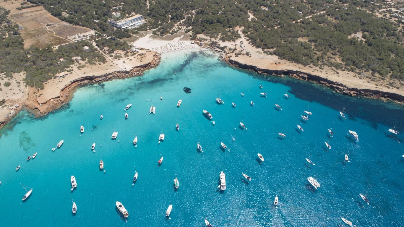 Muchos barcos sobre el mar turquesa y pequeños acantilados en Cala Saona.