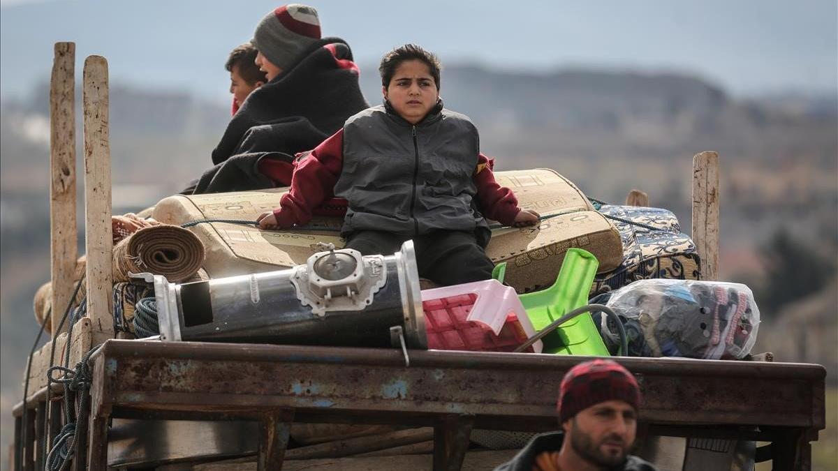 Desplazados sirios se sientan en la parte trasera de un camión con sus pertenencias huyendo de la ciudad de Idlib.