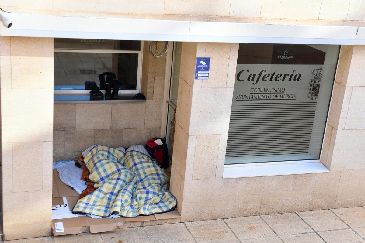 Dos personas bajo una manta en el exterior de la cafetería del Moneo, edificio municipal en pleno centro de Murcia.