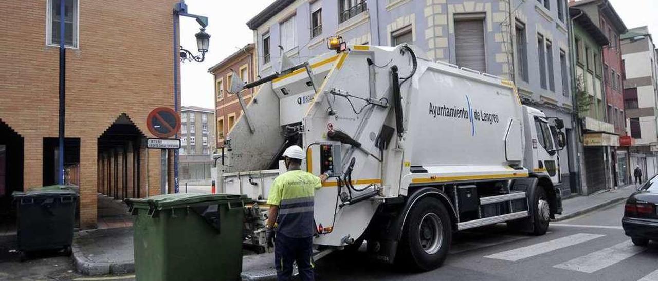 Un operario vacía un contenedor en un camión de recogida de basura en Sama.