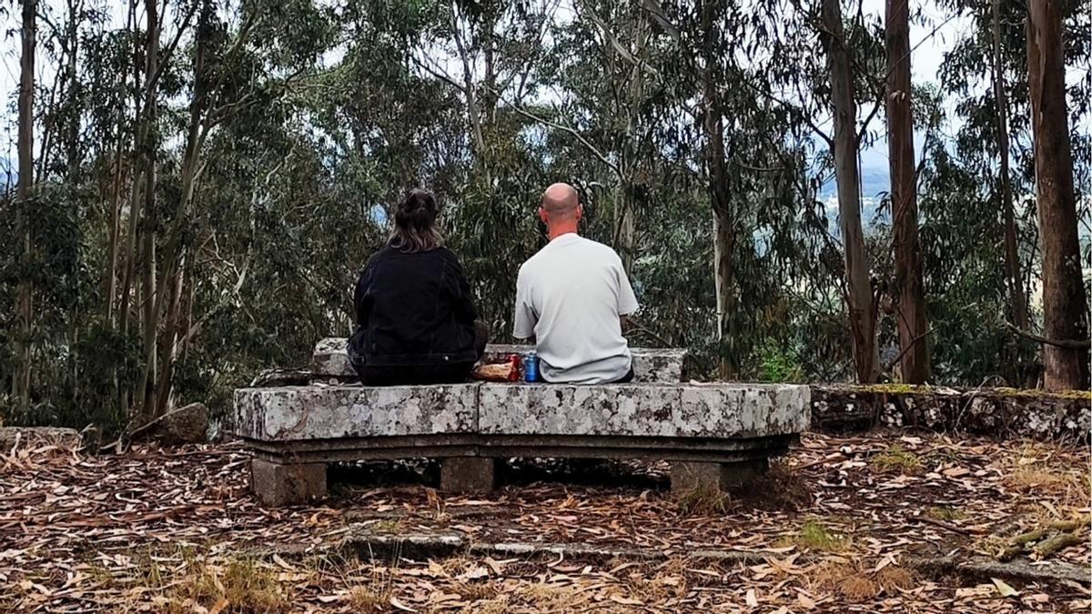 Dos personas sentadas en un banco del mirador de A Espenuca, totalmente oculto por los eucaliptos.