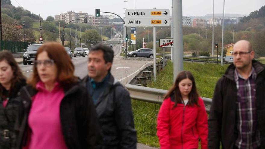 Peatones en La Vegona, con la nueva señal que indica La Plata y Avilés tras ellos.