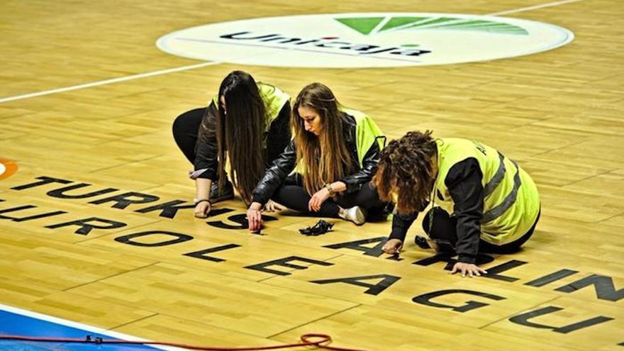 Voluntarias del Unicaja quitan del parqué del Palacio de los Deportes las pegatinas de los partidos de la Euroliga.