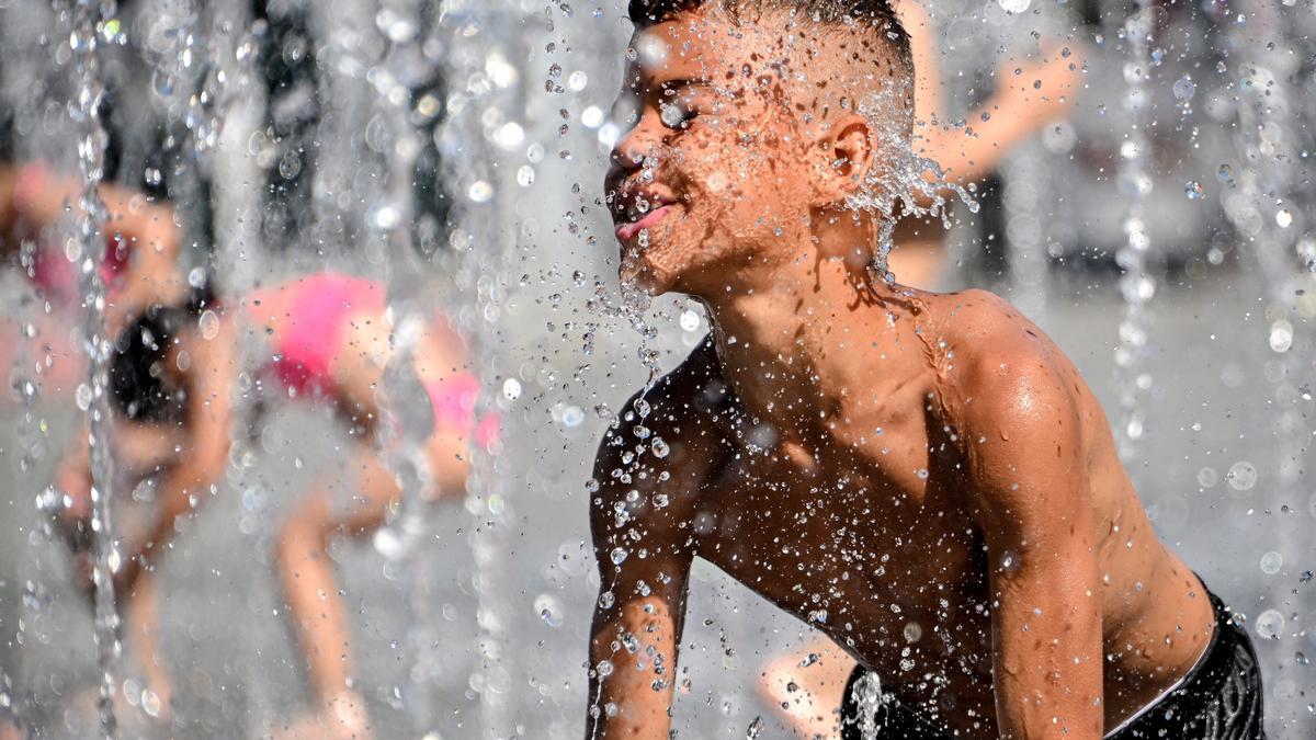 Unos chicos se refrescan en una fuente.