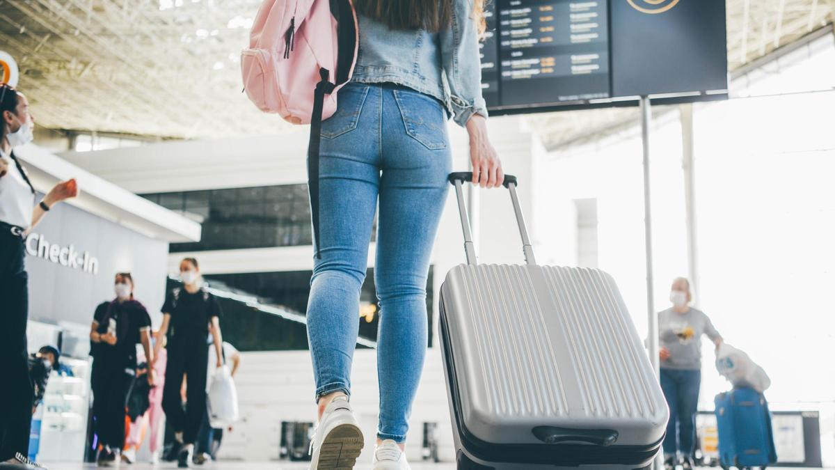 Una chica camina por el aeropuerto con su maleta de mano