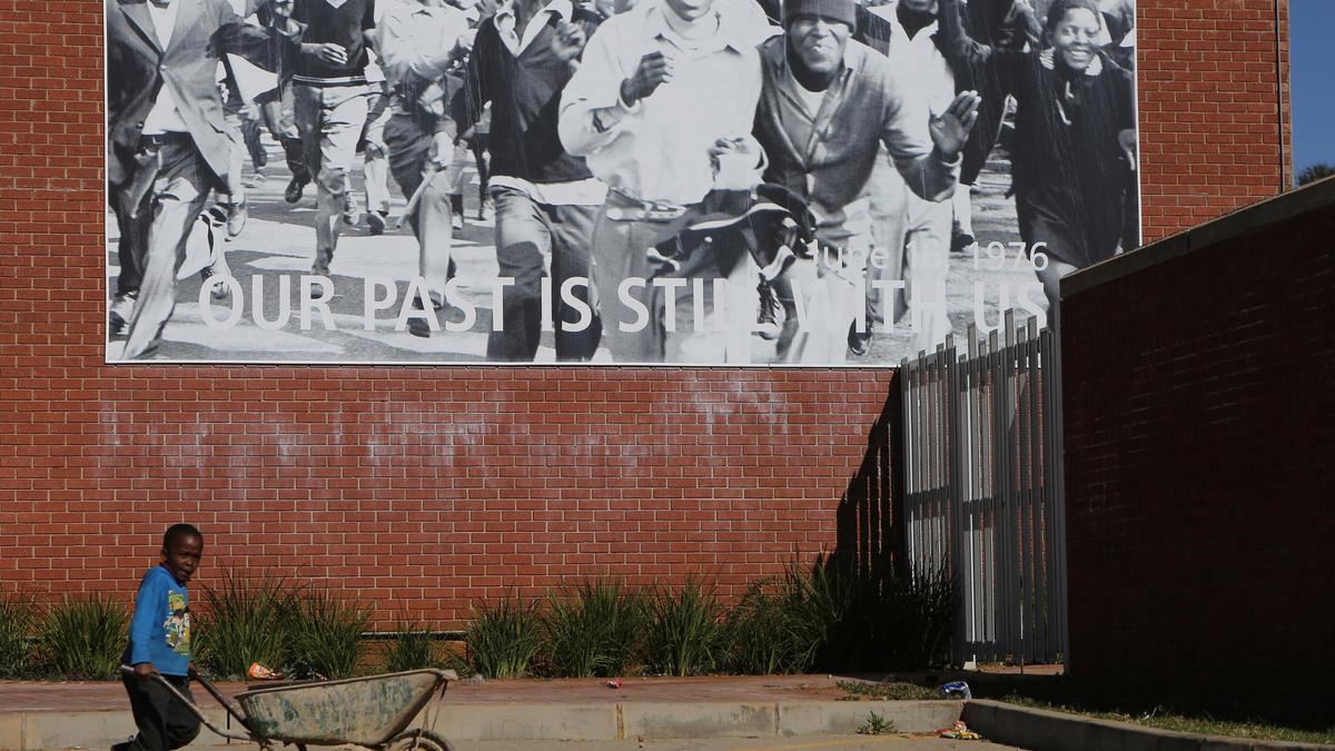 Un niño empuja una carretilla debajo de una fotografía gigante del fotógrafo Peter Magubane exhibida en un museo frente a la escuela Isaac Morrison en Soweto.