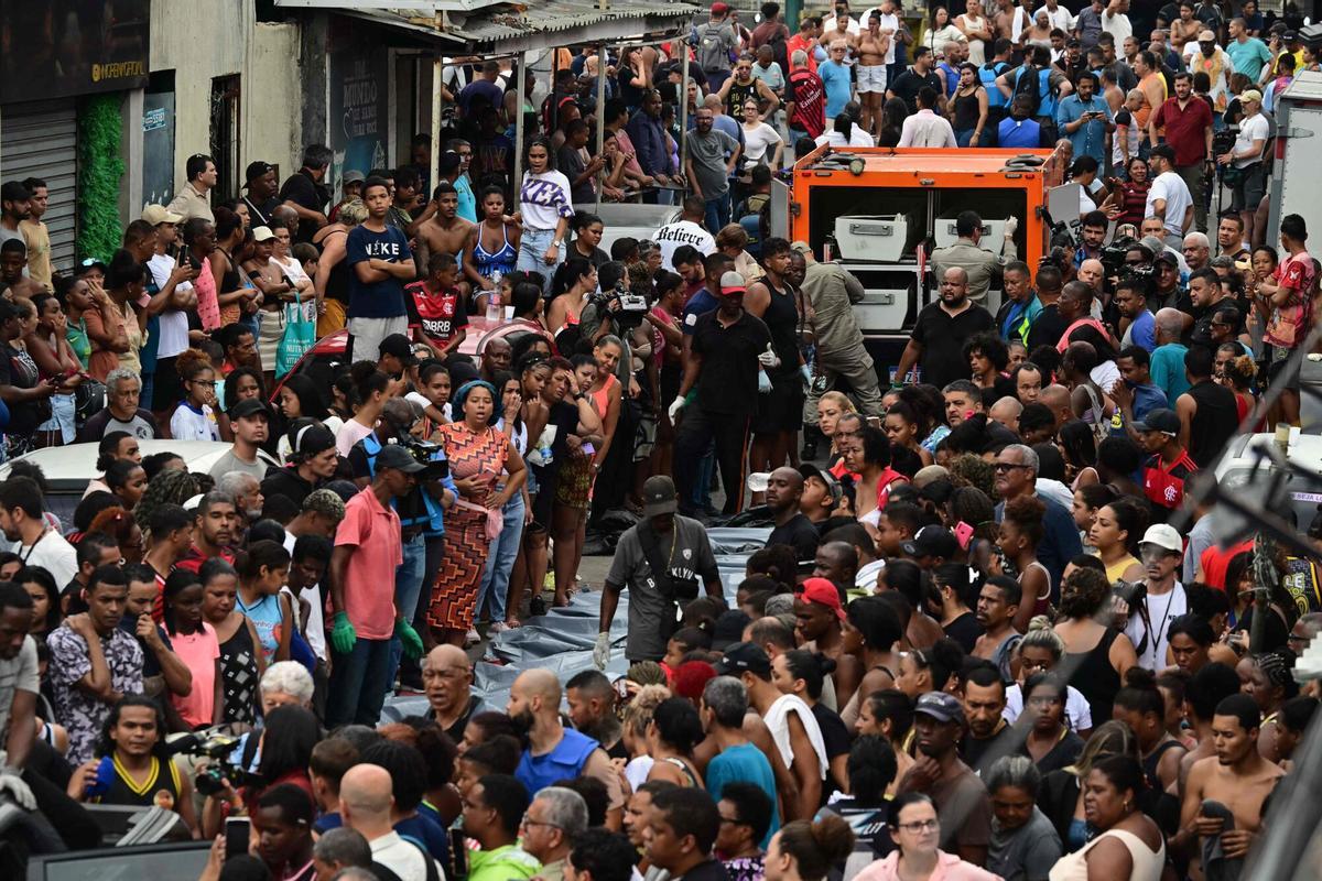 Residents stand next to lined-up bodies in front of a morgue truck on Sao Lucas Square of the Vila Cruzeiro favela at the Penha complex in Rio de Janeiro, Brazil, on October 29, 2025, in the aftermath of Operacao Contencao (Operation Containment). Residents of a favela in Rio de Janeiro lined up more than 50 bodies at a plaza in their low-income neighborhood on Ocotber 29, a day after the bloodiest police operation in the citys history, AFP reported. (Photo by Pablo PORCIUNCULA / AFP)
