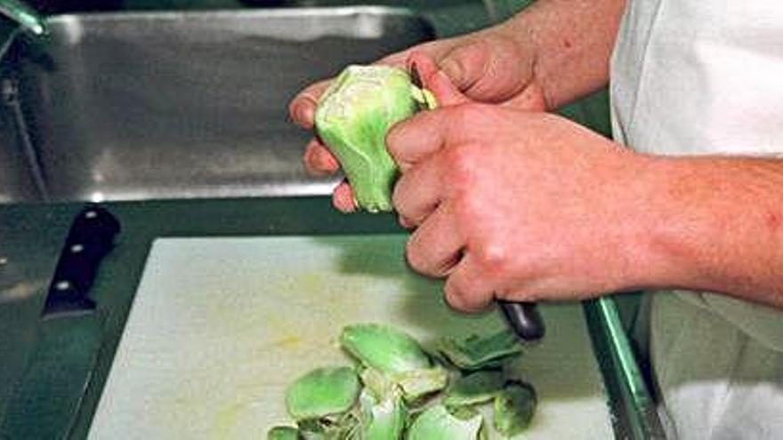 Un cocinero pela una alcachofa en una cocina.