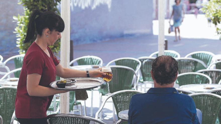 Una camarera sirve una cerveza y unas aceitunas a un cliente en una terraza.