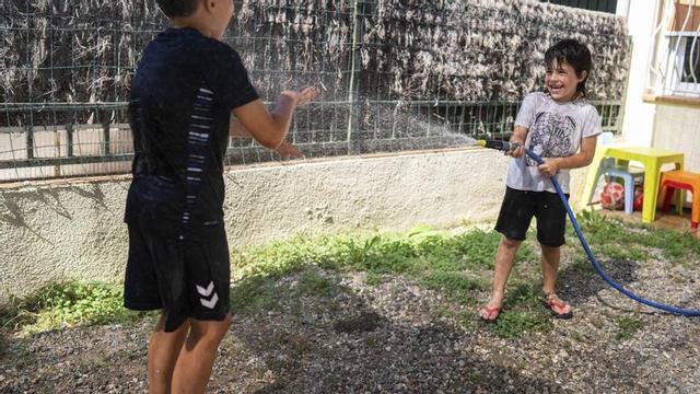 Dos germans es refresquen amb una manguera al pati de casa seva, a Sant Celoni (Vallès Oriental). | ZOWY VOETEN
