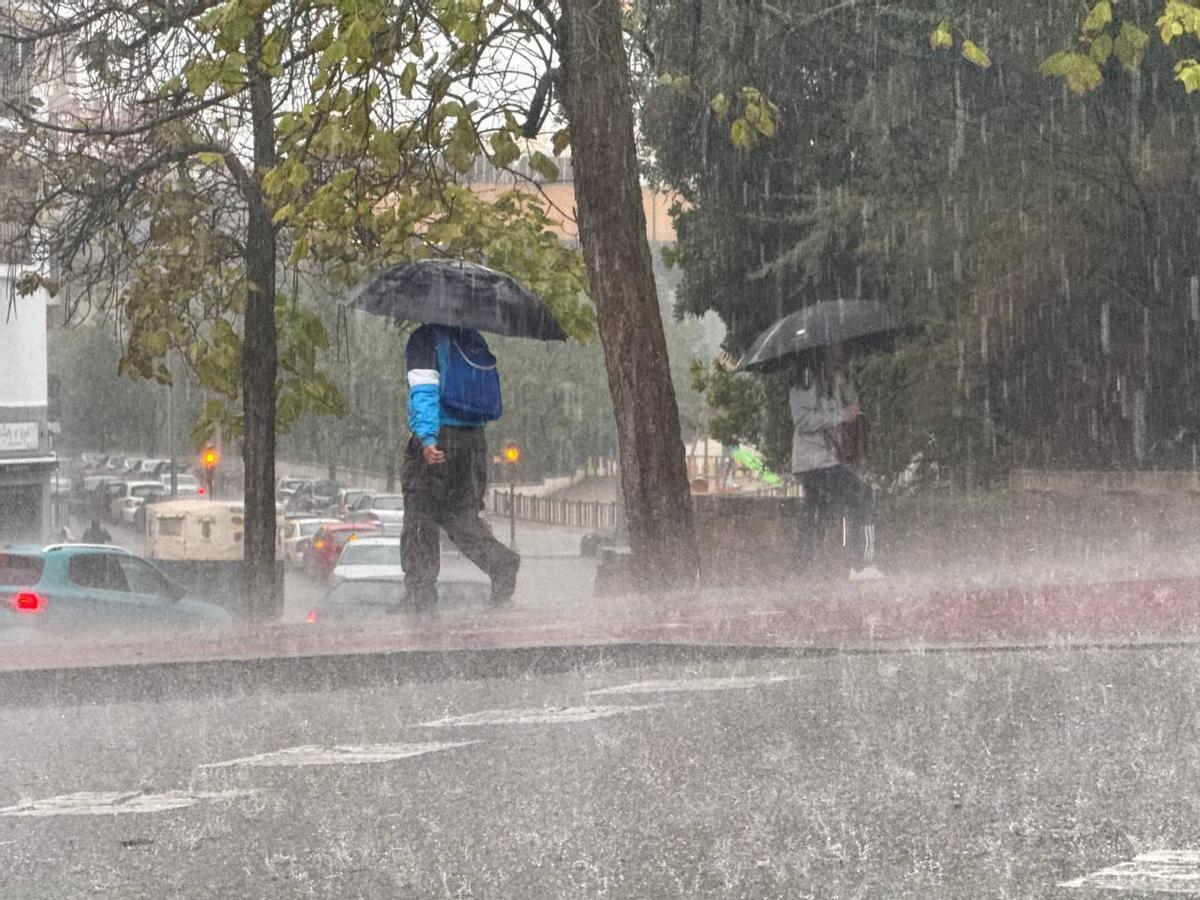 Dos personas intentan resguardarse bajo sus paraguas en medio de un gran aguacero.