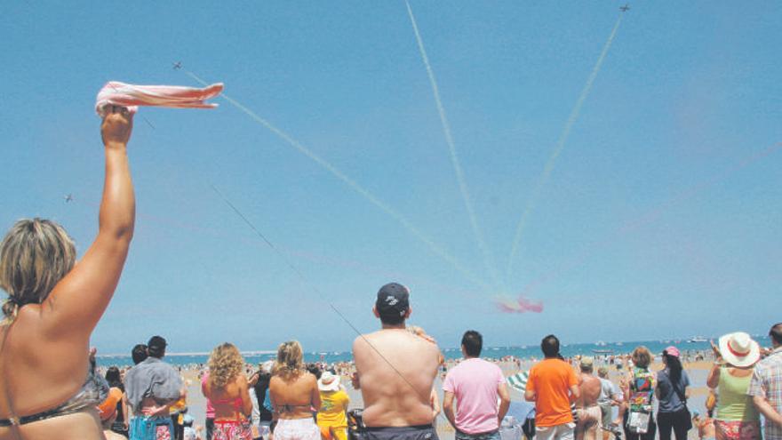 Unos bañistas saludan al paso de la Patrulla Águila, que deja los colores de la enseña española en el cielo gijonés.