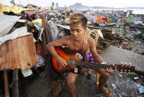 A survivor plays his guitar outside a makeshift shelter among the ruins of a residential neighbourhood devastated by super Typhoon Haiyan in Tacloban city